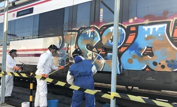 Operarios limpian un grafiti en un tren de Cercanías de Madrid.